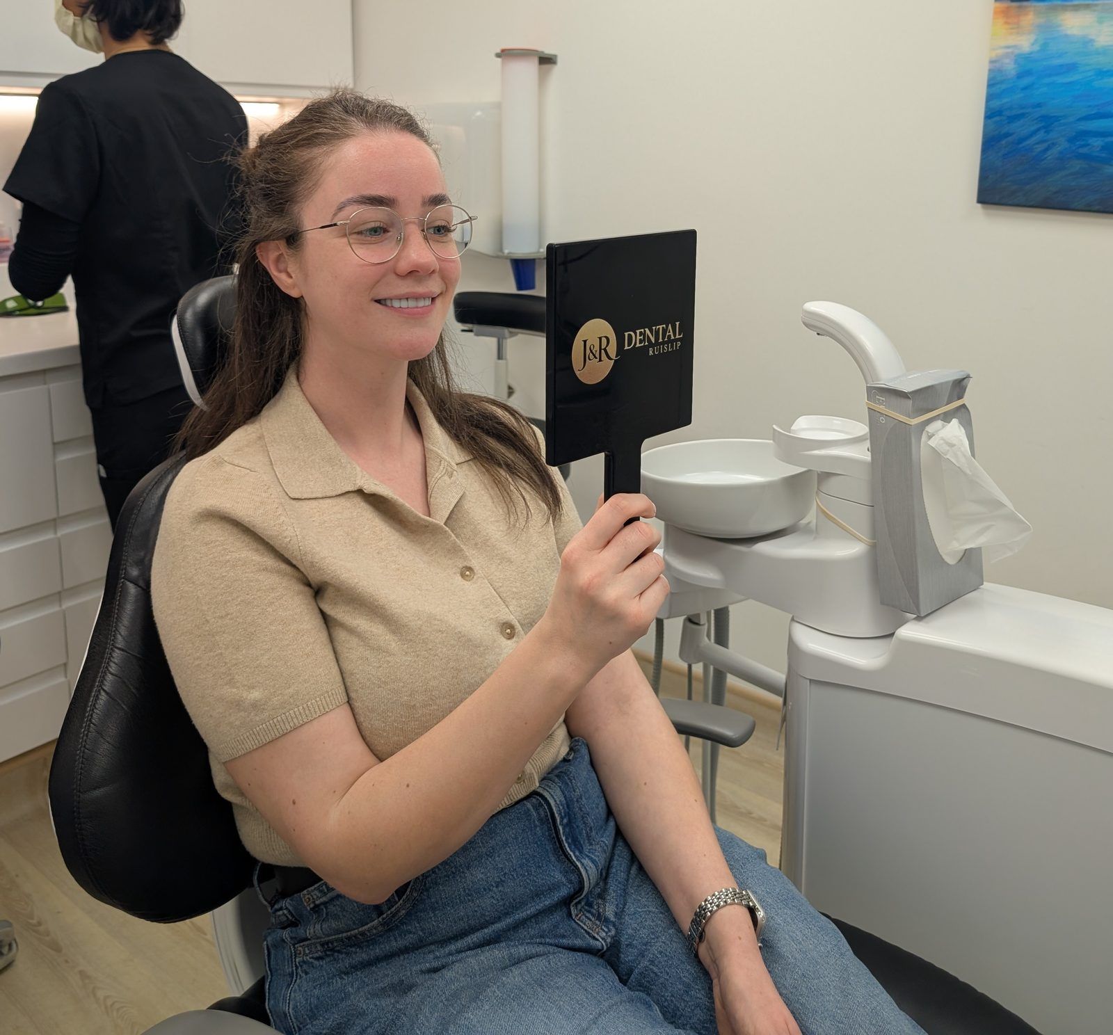 Happy patient at J&R Dental Ruislip admiring her smile in a branded mirror after Invisalign treatment.